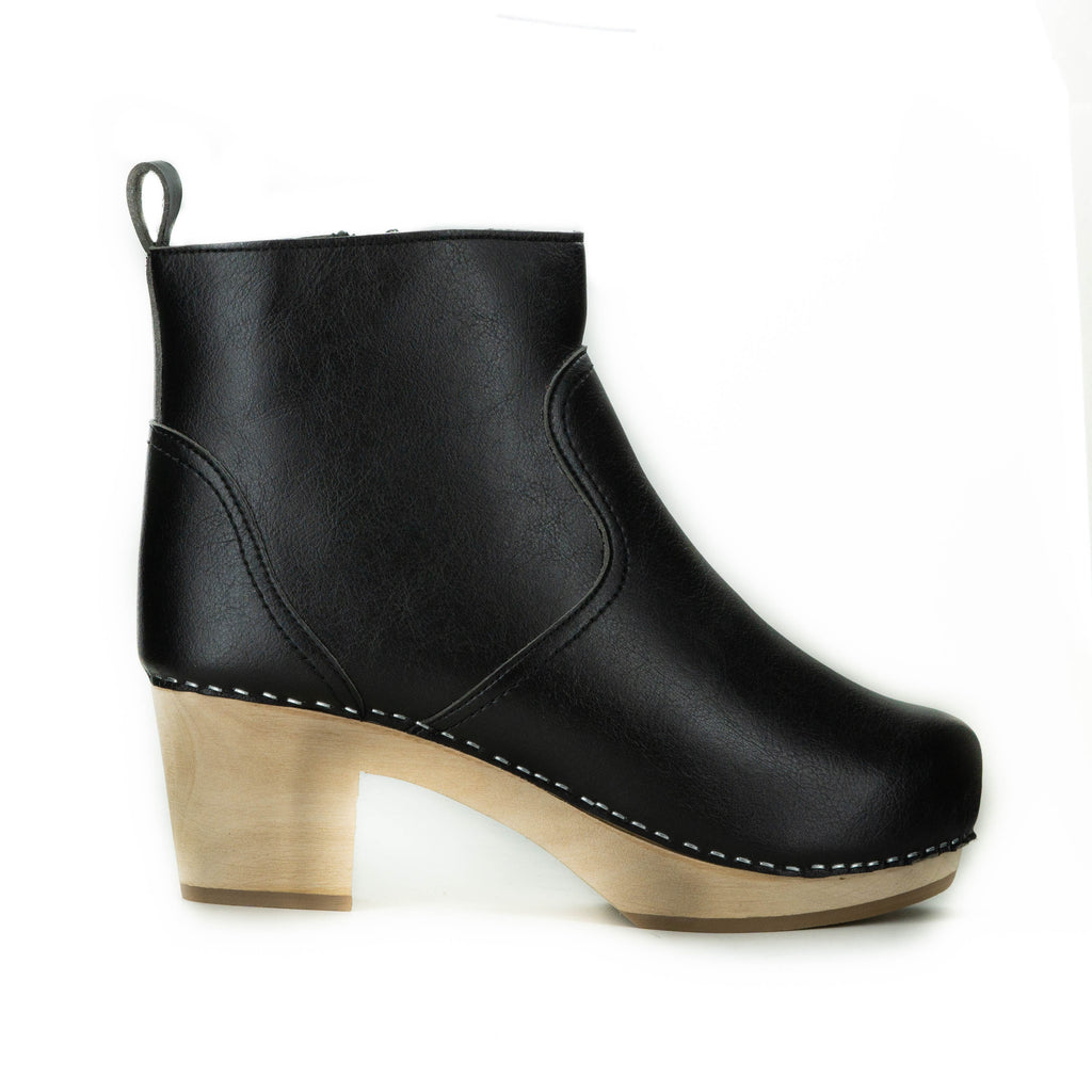 A black vegan leather clog bootie. Ankle height shaft with pull tab in back. Inside zipper closure. Blonde wooden sole. Staples around outsole to connect material to sole.