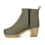 A taupe vegan suede clog bootie. Ankle height shaft with pull tab in back. Inside zipper closure. Blonde wooden sole. Staples around outsole to connect material to sole.