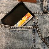 Small cardholder in black vegan leather. 2 card slots on each side and slot in middle. Shown here attached to a belt chain, in a back jean pocket.