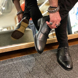 A black vegan leather men's dress shoe with a cap toe. Slightly tapered toe. Lace up with 5 eyelets. Black lining and sole. Shown on a man's feet with a mirror in the background to show the bottom of the sole.